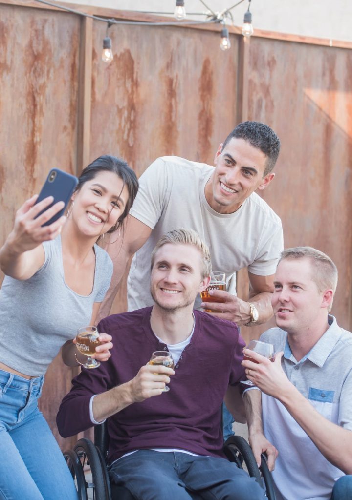 Eine Frau und drei Männer (einer sitzt im Rollstuhl) machen ein Selfie