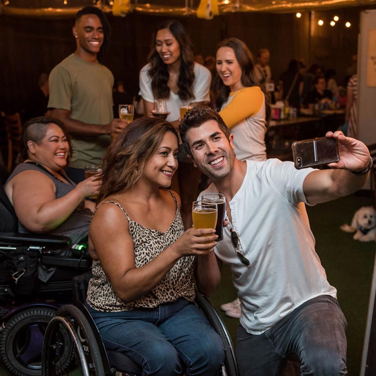 Four women (two are in a wheelchair) and two men taking a selfie dring a party.