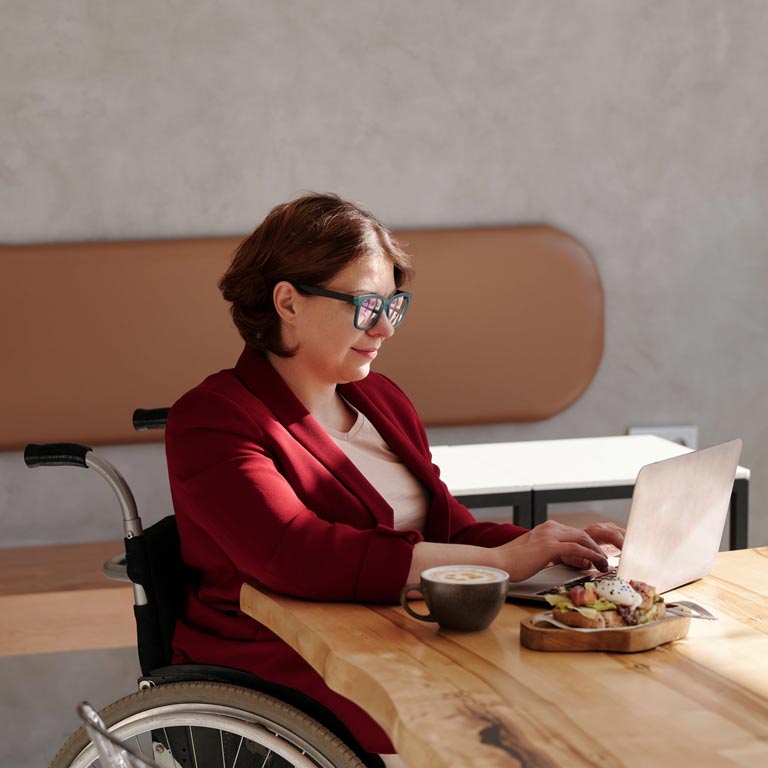 Eine Frau im Rollstuhl arbeitet in der Sonne an ihrem Computer